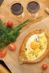 Khachapuri in Adjarian. Open pie with oriental cheeses and egg. Homemade baking. Georgian cuisine. Two glasses with red wine