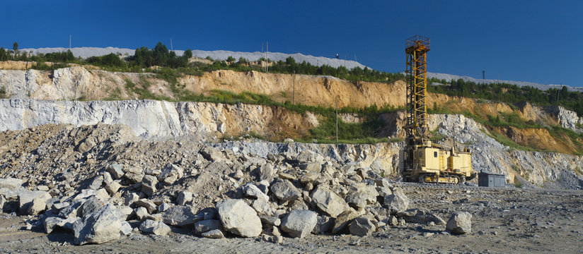 Quarry drilling rig inside the quarry on the background of the wreckage of stone ore and blue sky, panorama. Heavy mining equipment. - Powered by Adobe