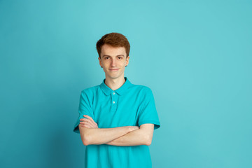 Hands crossed. Caucasian young man's modern portrait isolated on blue studio background, monochrome. Beautiful male model. Concept of human emotions, facial expression, sales, ad, trendy.