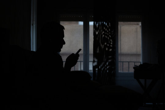 silhouette of a man looking at his cell phone at home