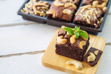 Chocolate brownies with cashew nut and papermint on wooden plate on white wooden floor with...