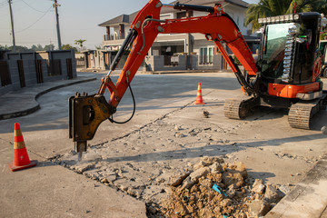 Excavator breaking concrete road surface with hydrohammer drill at repairing roadwork.