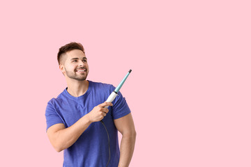 Handsome young man with curling iron on color background