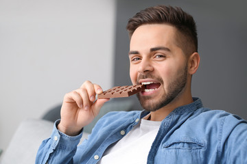 Handsome young man eating chocolate at home