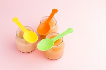 Closeup of jars of baby food with colorful spoons on pink background