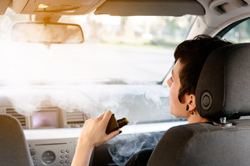 young woman vaping inside a car. used an electronic cigarette to quit smoking. Alternative to...