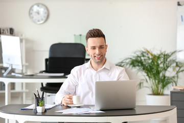 Man drinking coffee while working on laptop in office