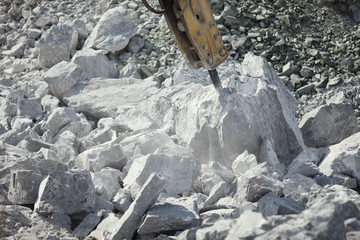 Crushing arm of a hydraulic hammer crushes large stone in a stone quarry, closeup. Heavy mining equipment.