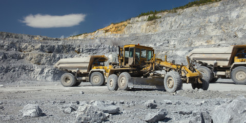 Wheeled quarry tractor with a scraper works in a quarry for limestone mining, panorama. Heavy mining equipment.