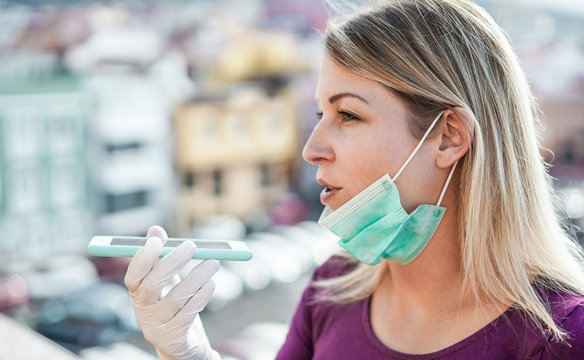 Young woman sending voice message outdoor during isolation quarantine - Girl using social app while wearing face mask and latex gloves for Covid-19 prevention - Focus on hand