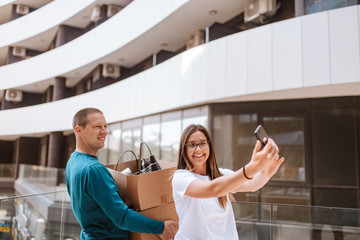 Beautiful caucasian man and woman taking selfies in front of building. Love and moving