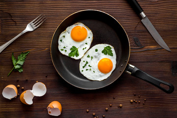 Fried eggs on frying pan on wooden background top view