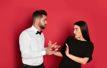 Young woman rejecting engagement ring from boyfriend on red background