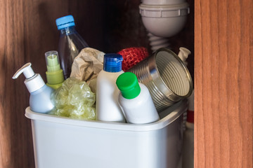 Plastic trash can in the kitchen cabinet - bottles, plastic and metal cans in the trash bin in the kitchen.