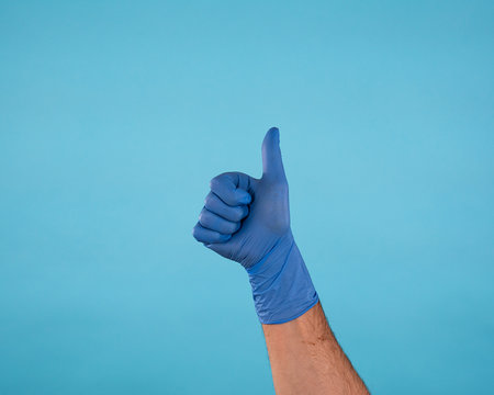 Male Hand In Blue Surgical Latex Gloves Making Thumbs Up Gesture Isolated On Blue Background