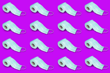Rolls of toilet paper and medical masks in rows on a purple background.