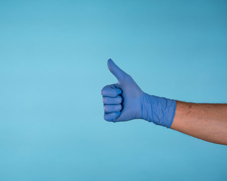 Male Hand in blue surgical latex gloves making thumbs up gesture isolated on blue background
