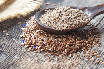 Crushed flax seed in a wooden spoon on a pile of flaxseed.