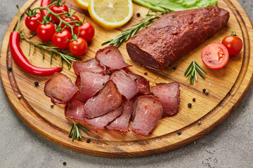 Armenian basturma or Pastirma on wooden cutting board decorated with spices, lettuce, lemon and tomatoes. Meat smoked jerky good as Beer snack
