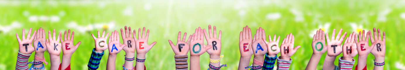 Children Hands Building Colorful English Word Take Care For Each Other. Sunny Green Grass Meadow As Background