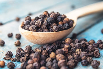 Dry black pepper in a wooden spoon near black pepper scattered on blue boards.