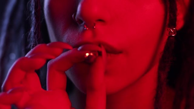 smoking cannabis closeup, girl smokes marijuana in a dark room in neon light. tattoos and dreadlocks