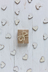 Handmade gift in kraft paper on a white background. Wooden decorative hearts around gift.