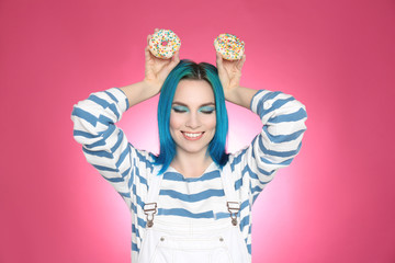 Young woman with bright dyed hair holding donuts on pink background