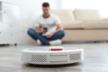 Fototapeta premium Man resting while robotic vacuum cleaner doing his work at home
