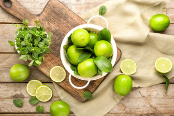 Colander with fresh limes and mint on wooden background