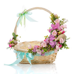 Fototapeta na wymiar Floral decor on the handle of a wicker basket. Decor with pink flowers, greens, quail eggs and bows made of blue ribbons on white background