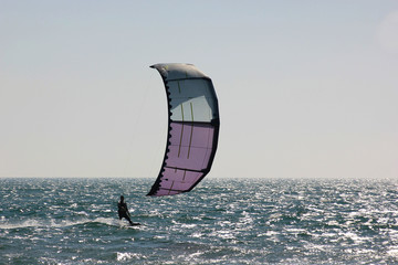 blue-violet sail of a kite close up on the background of the sea with a small black figure of a man