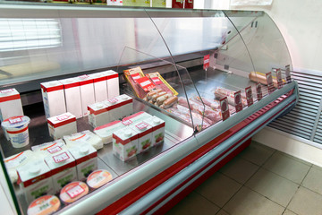 Counter with milk and sausage in store. Refrigerator shelves with different products