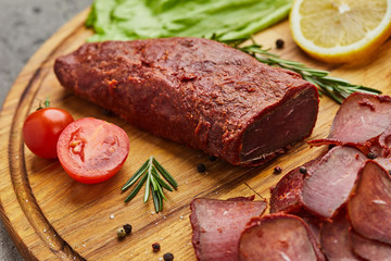 Armenian basturma or Pastirma on wooden cutting board decorated with spices, lettuce, lemon and tomatoes. Meat smoked jerky good as Beer snack