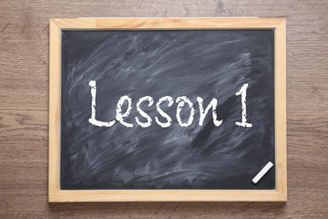 Blackboard with phrase LESSON 1 on wooden background, top view