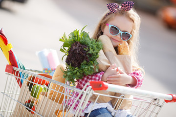 Adorable baby kid with trolley choosing fresh vegetables in local store. Girl with a big grocery...