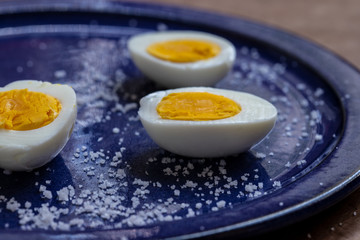 three half eggs on a blue plate with salt