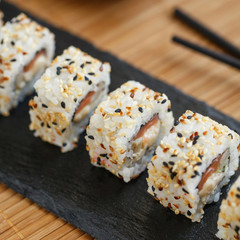 Uramaki served on a black slate with wooden black sticks and soy sauce. Japanese traditional food with bamboo service.