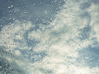 Wet window with rain drops and a cloudy sky outside.