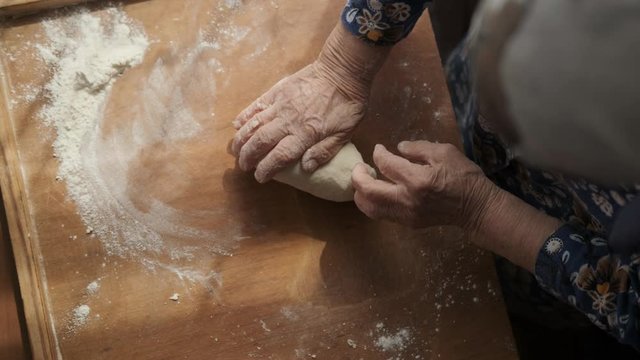Shot from above: an elderly woman kneads soft dough for home baking.