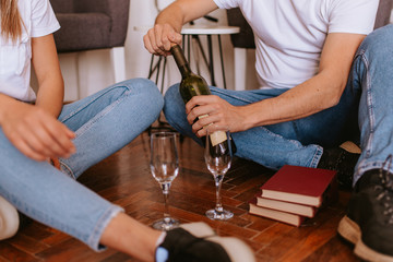 An attractive caucasian man and woman are sitting on the floor of a new apartment, drinking wine and celebrating. A loving couple moves in