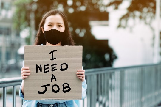 An unemployed women holding a paper sign writing a message saying she needs a job