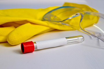 Test tube with a tuffer on the background of rubber gloves and glasses on the table. Covid-19 on a...