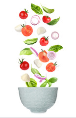 Mozzarella cheese, tomatoes, onion and basil leaves falling into bowl on white background