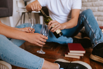 Fototapeta na wymiar An attractive caucasian man and woman are sitting on the floor of a new apartment, drinking wine and celebrating. A loving couple moves in