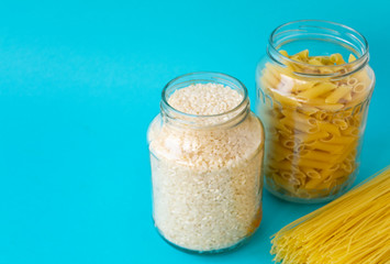 Noodles, rice, pasta in glass jars stand on a blue background. Raw materials for cooking.