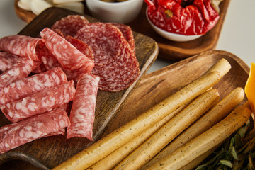 High angle view of salami slices, breadsticks and antipasto ingredients on boards on white background