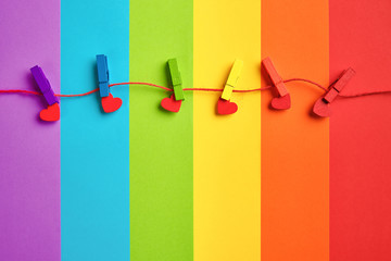 rainbow colored wooden clothespins with clamped red hearts on lgbt flag background.