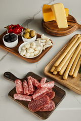 High angle view of boards with breadsticks, salami slices, cheese and antipasto ingredients on white