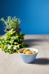 selective focus of parsley and olives in bowl on wooden table on blue background